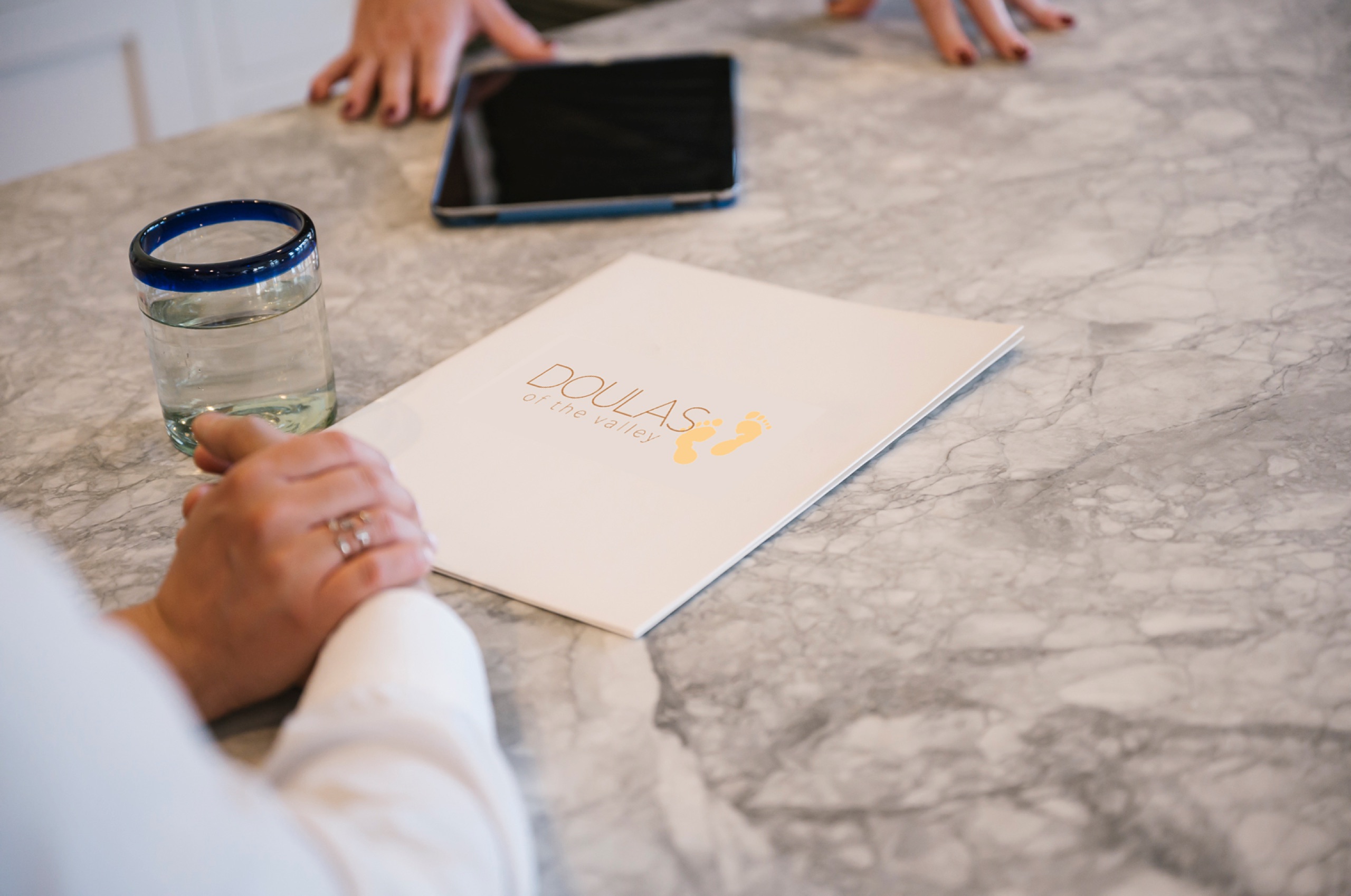 Hands resting beside a Doulas of the Valley folder and a tablet on a kitchen counter