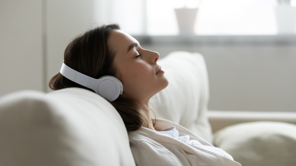 A woman resting with her eyes closed and headphones on, lying back on a couch