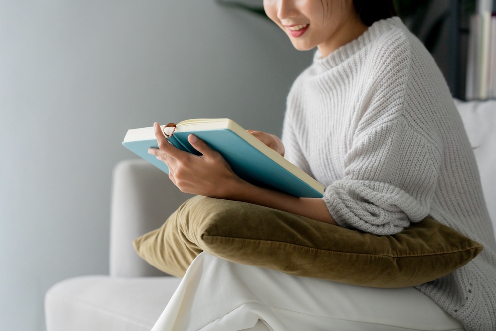 A woman in a soft sweater sitting on a couch reading a book